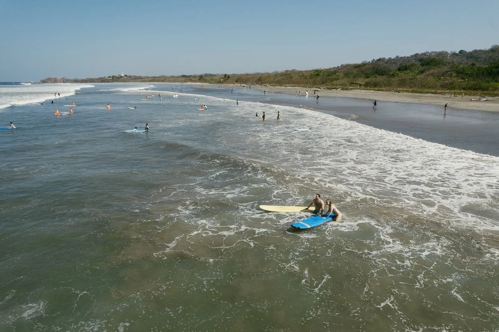 A surfer paddling out on a long, empty stretch of beach in Nosara