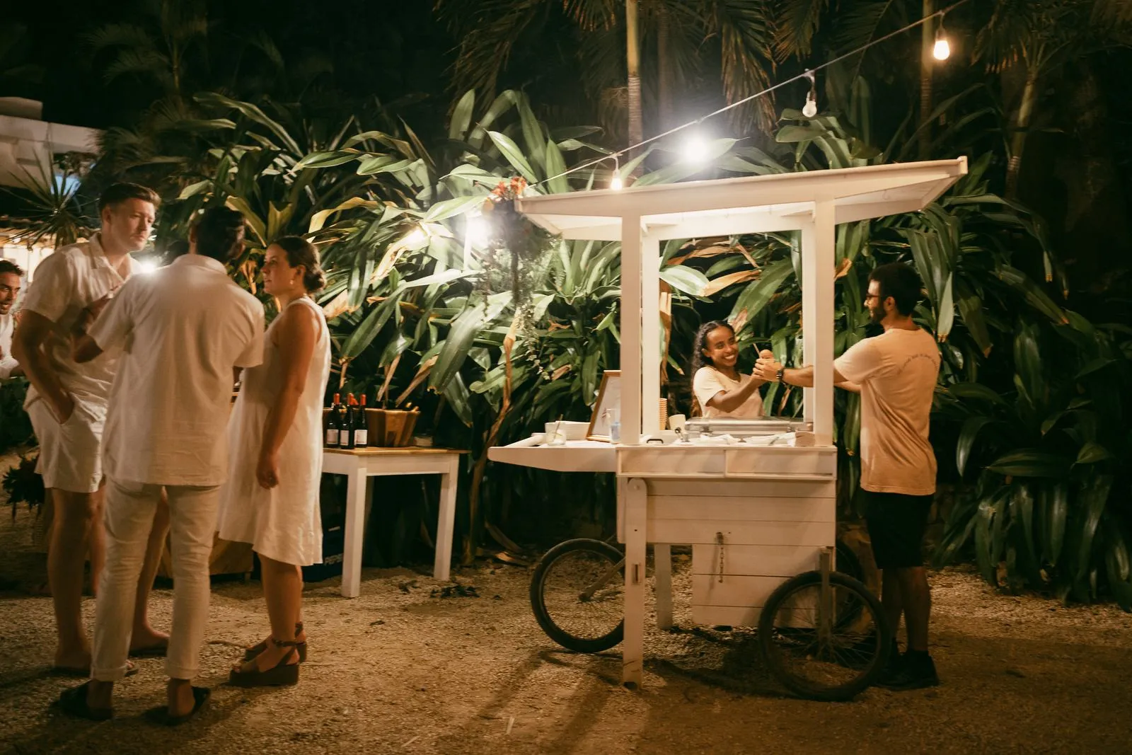 Guests gathered around a white ice cream cart under festoon lights at a Nosara welcome party