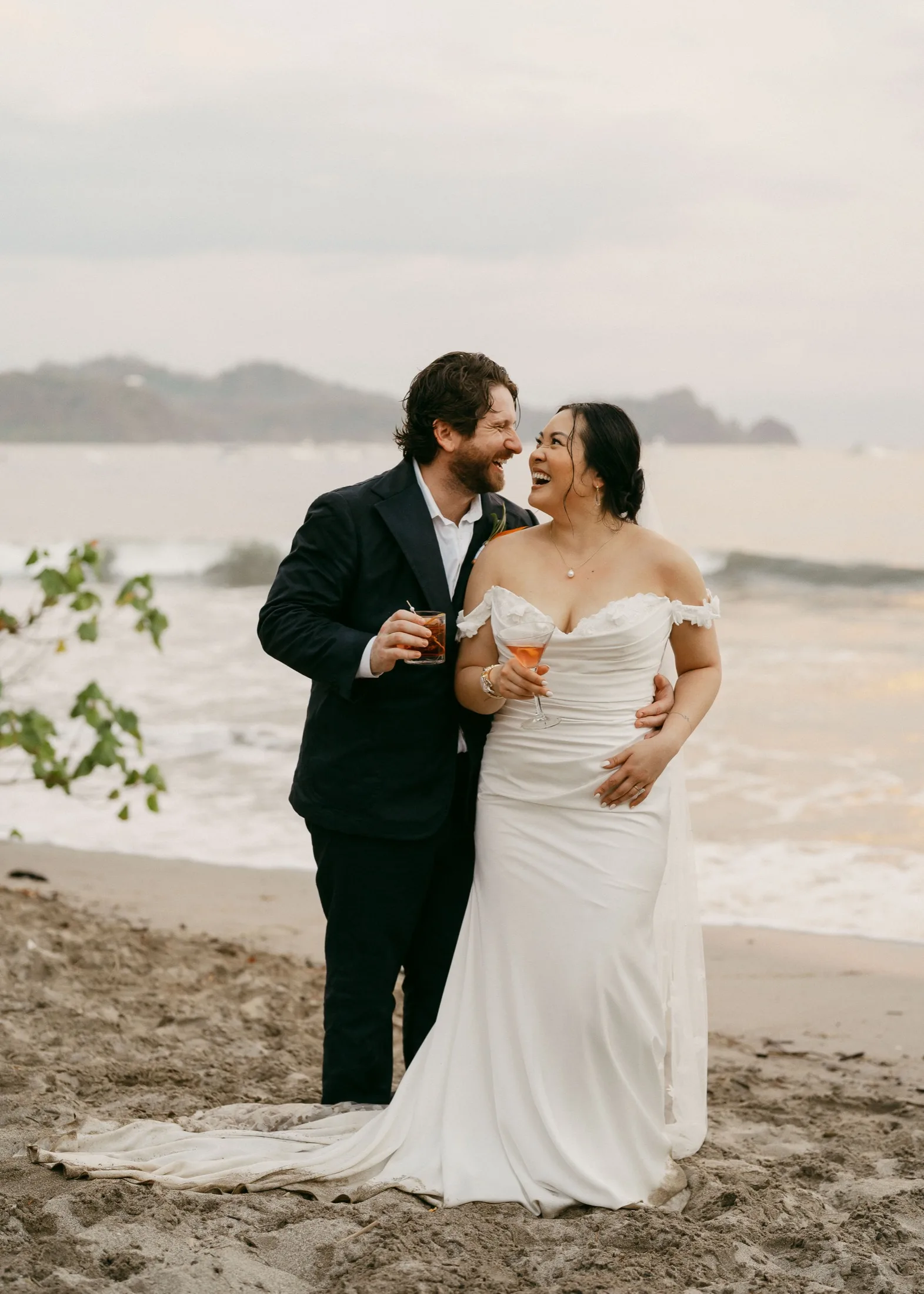 A newly married couple laughing together on the beach at Nosara under a soft grey sky