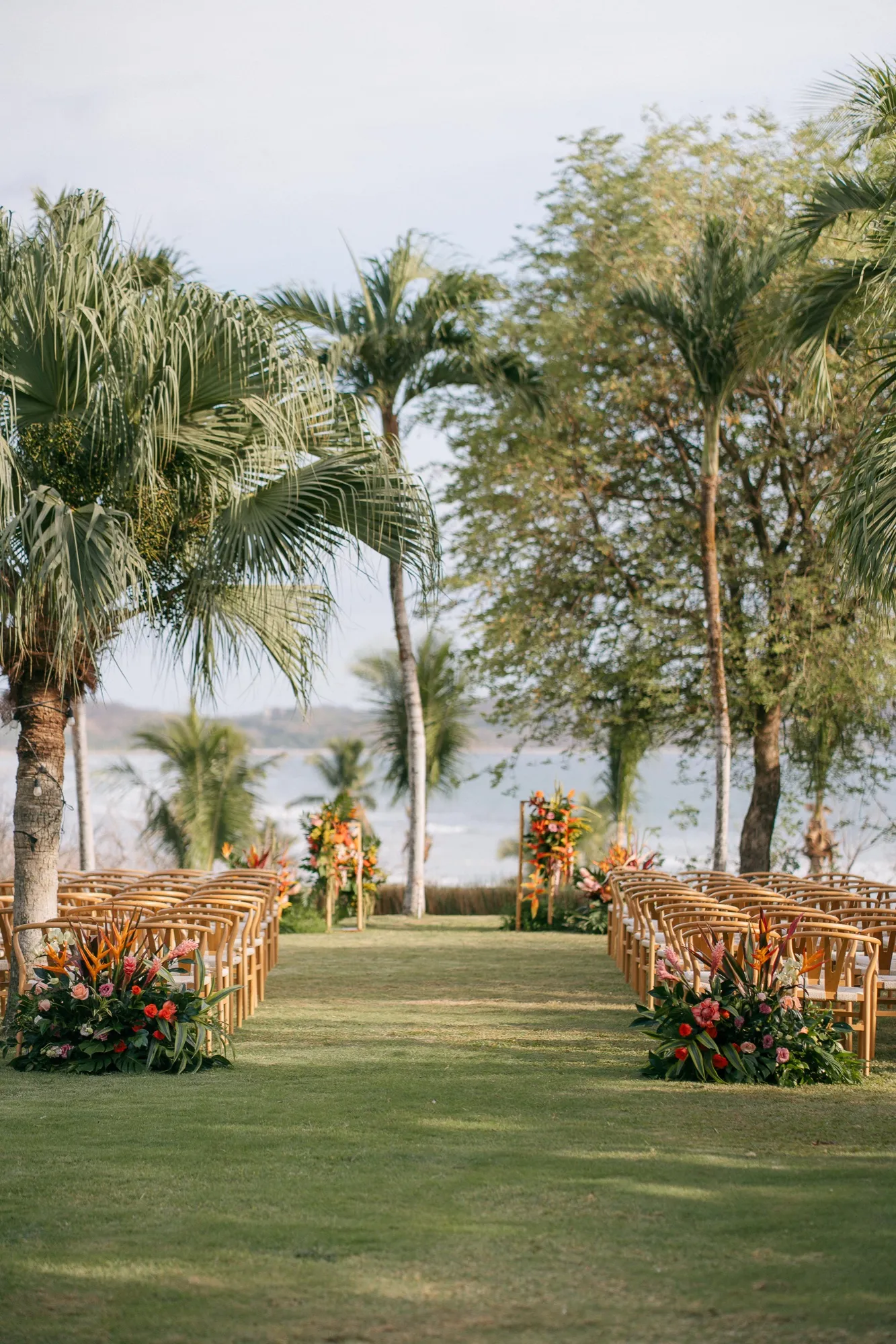 A ceremony aisle lined with tropical florals and palms overlooking the ocean in Nosara
