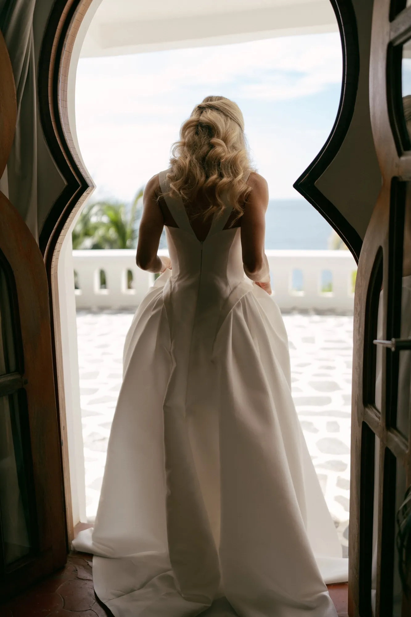 A bride in a ballgown framed in an archway with the ocean beyond