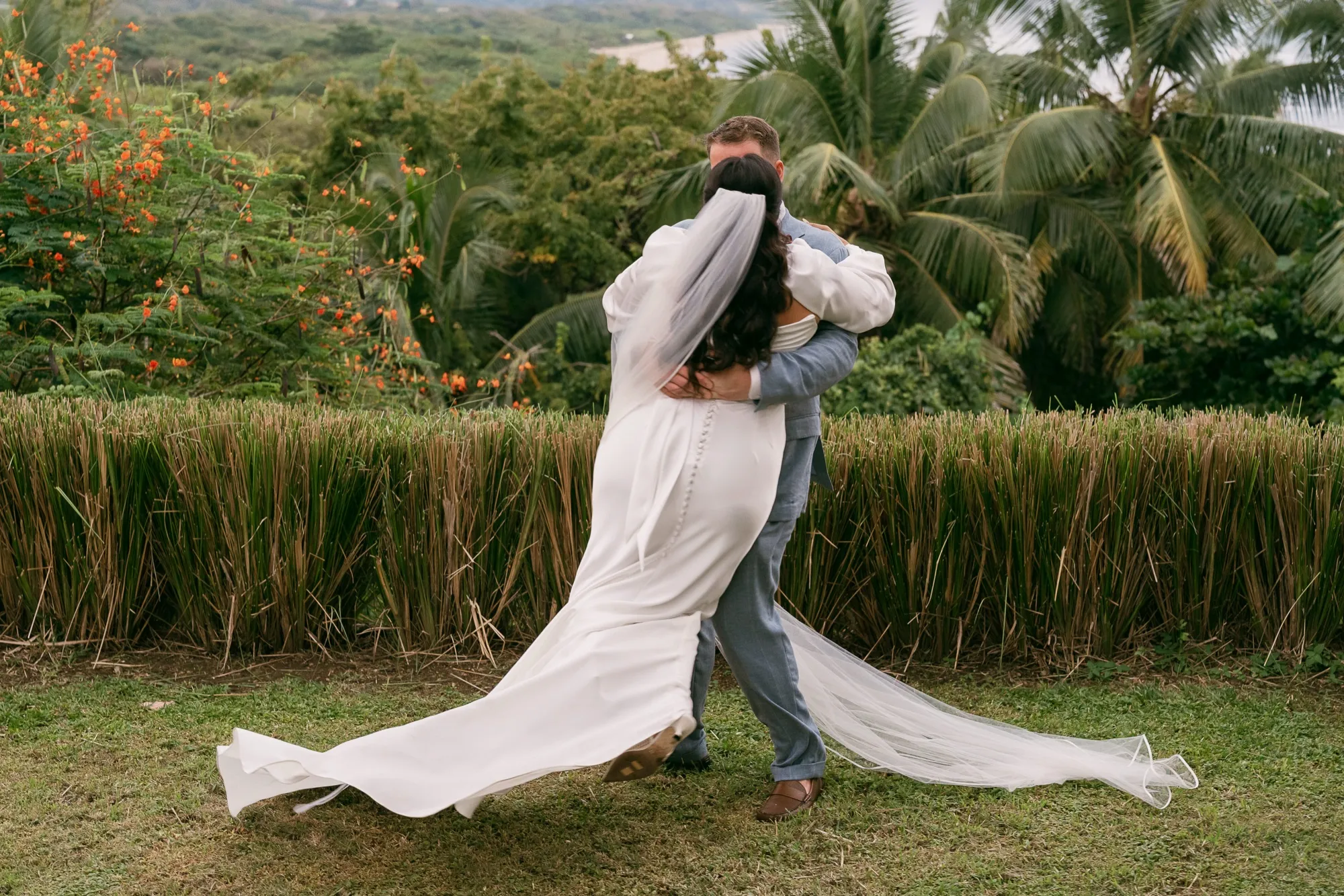 A groom dipping his bride for a kiss in the jungle, her veil swirling