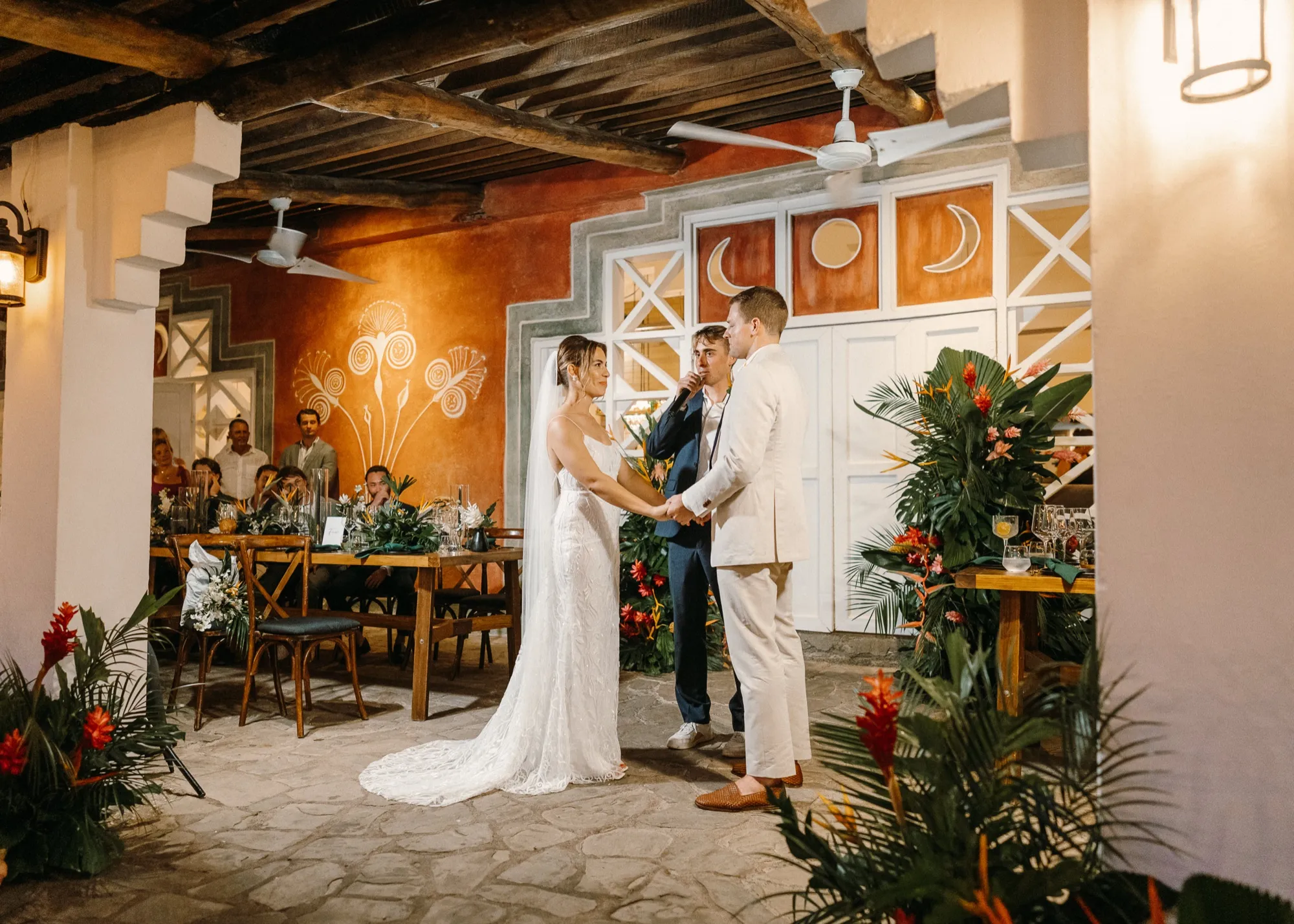 A couple exchanging vows on a terracotta veranda framed by tropical florals