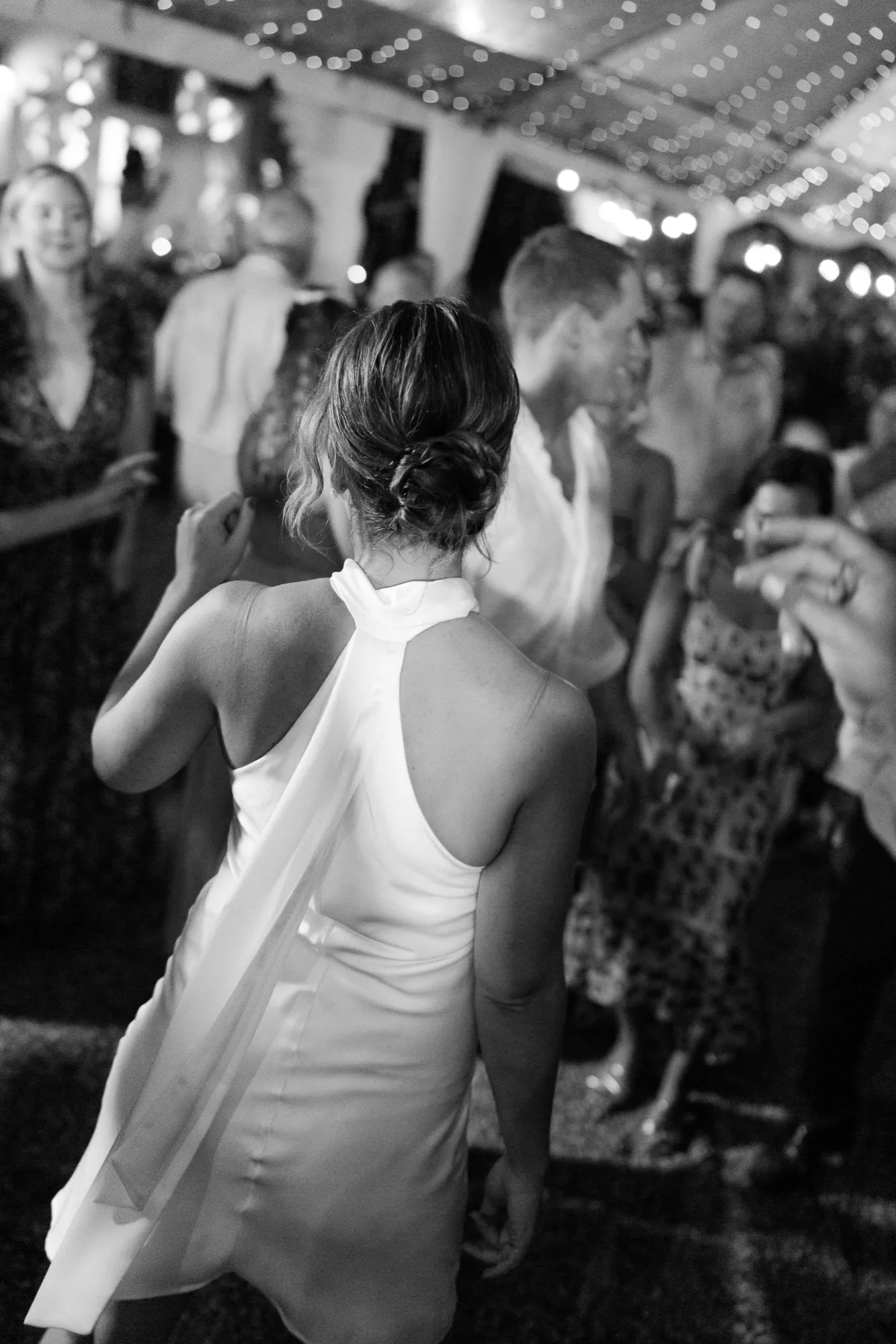 A bride dancing under string lights at the reception, in black and white
