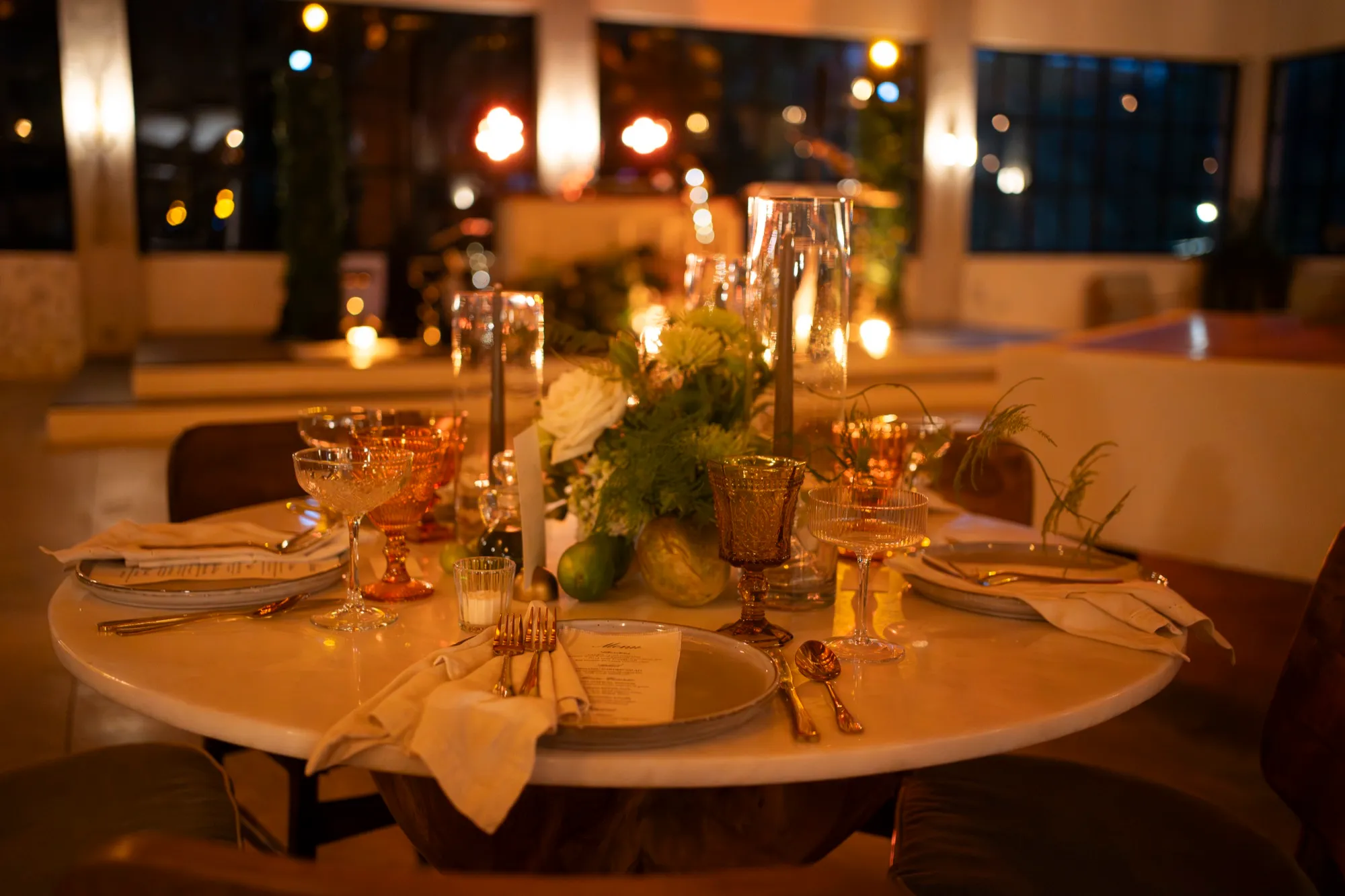 A candlelit reception table set with amber glassware and white florals at night