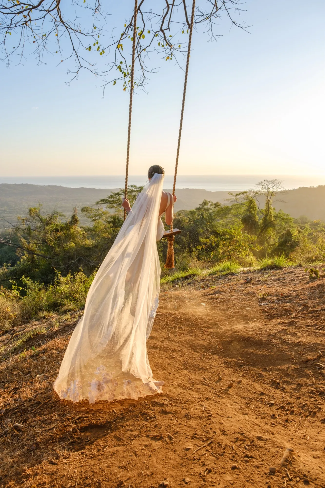 A bride on a swing at golden hour overlooking the Nosara jungle and ocean, veil flowing