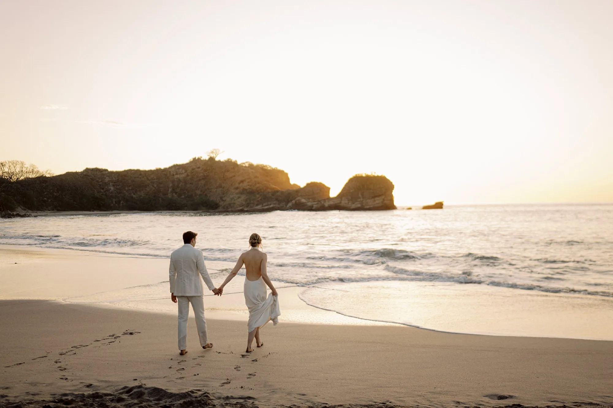 Newlyweds walking hand in hand along the beach at sunset in Nosara