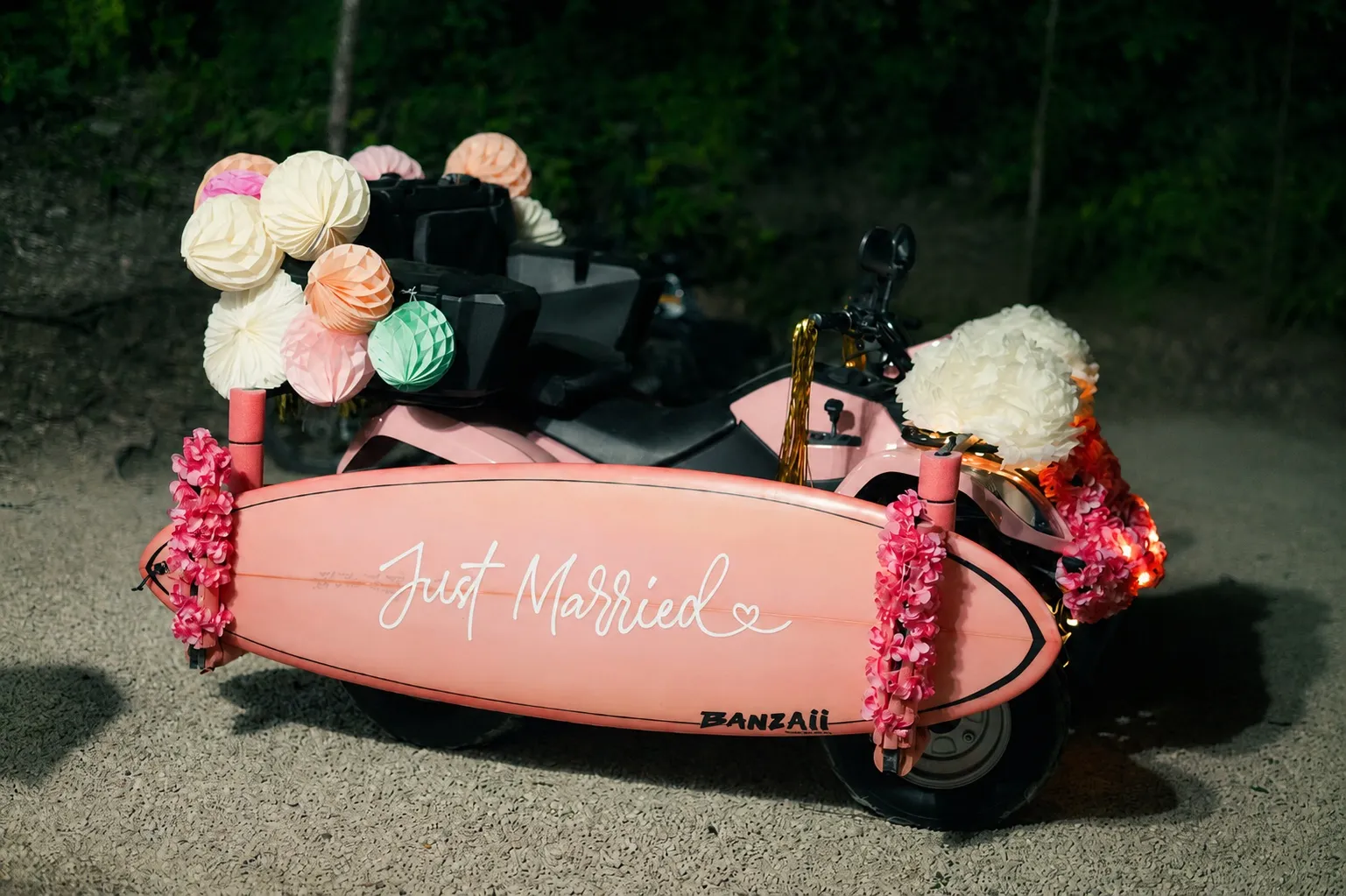 A pink motorbike sidecar decorated with paper lanterns and a surfboard painted Just Married, waiting for the send-off