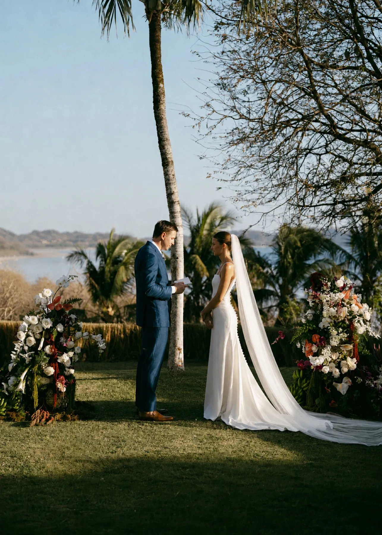 A couple exchanging vows beneath the palms above the ocean in Nosara, framed by two tropical floral pillars
