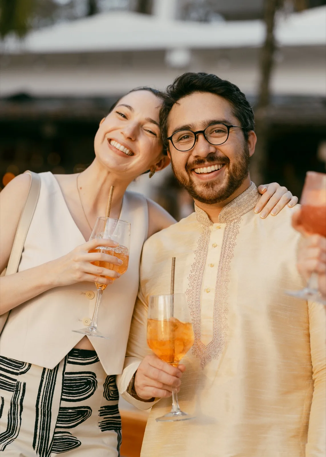 Two wedding guests laughing together with cocktails at a Nosara welcome dinner in golden light