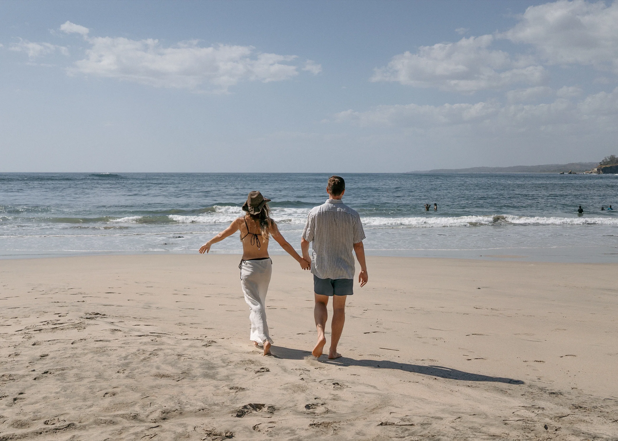 A couple walking hand in hand across the sand toward the Pacific on a wide, open beach in Nosara