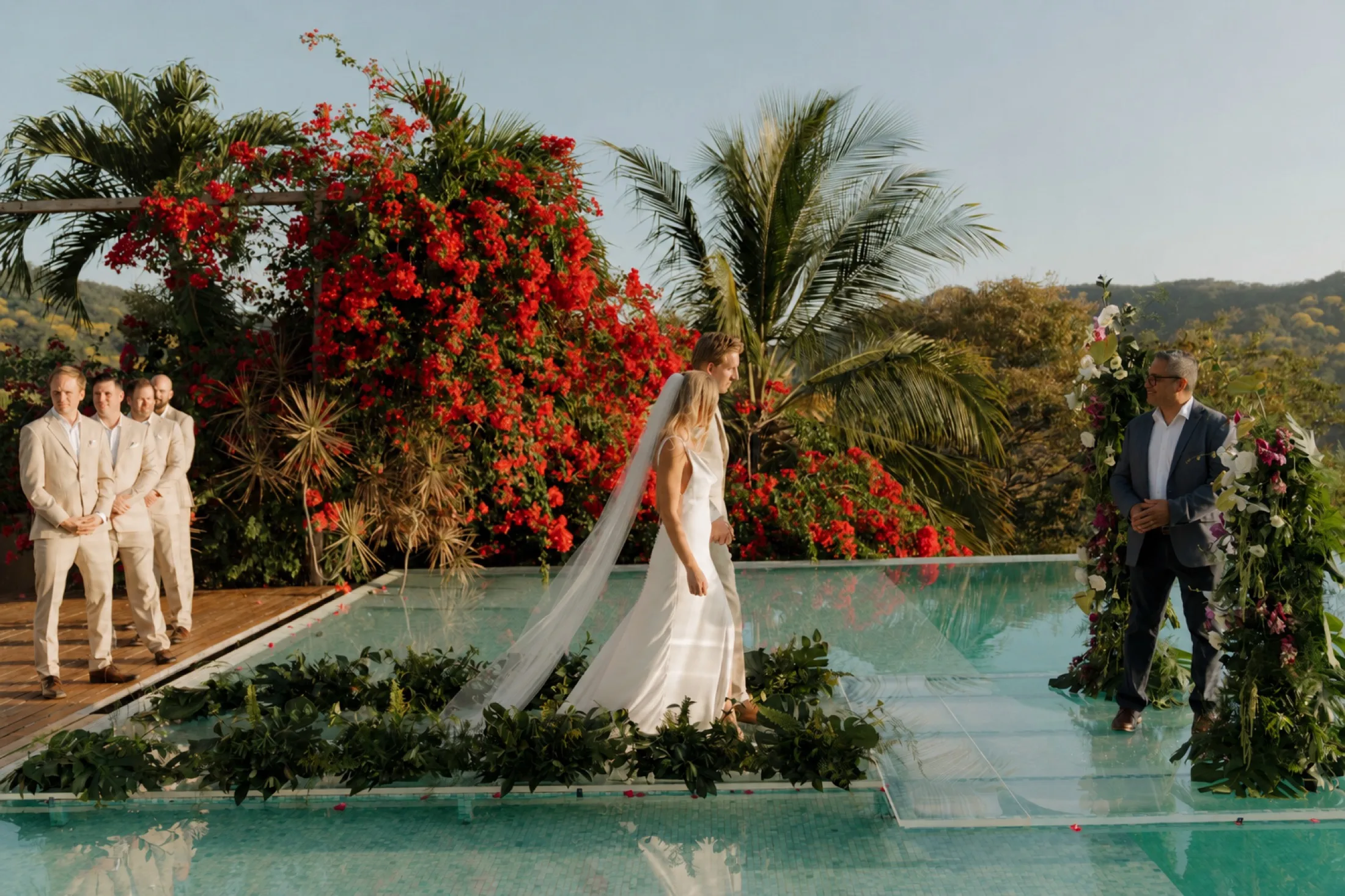 A bride crossing a glass platform over a pool at a jungle-and-bougainvillea wedding ceremony in Nosara, Costa Rica