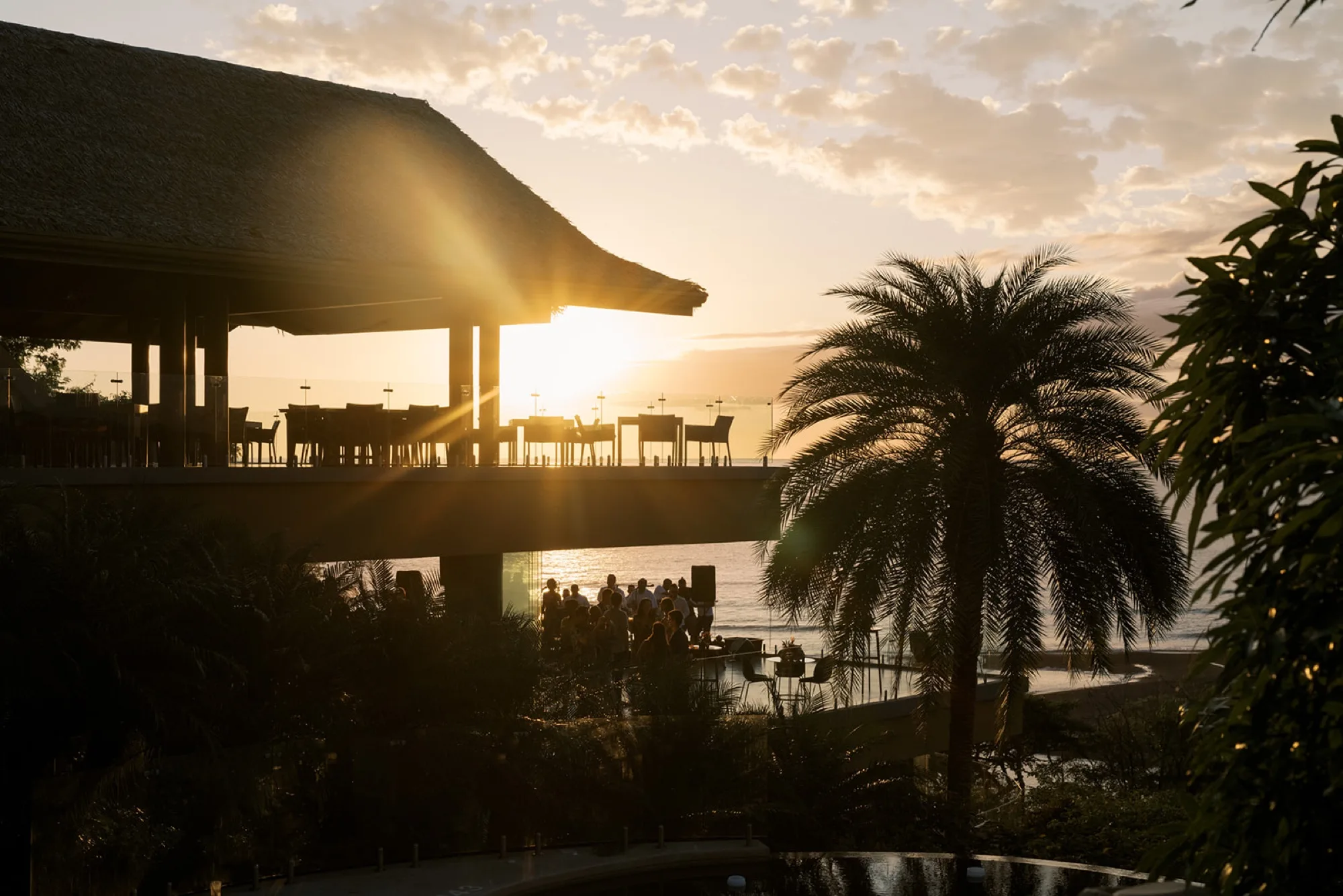 An open-air, thatched-roof venue above the Pacific at sunset in Nosara, with guests gathered on the lower terrace