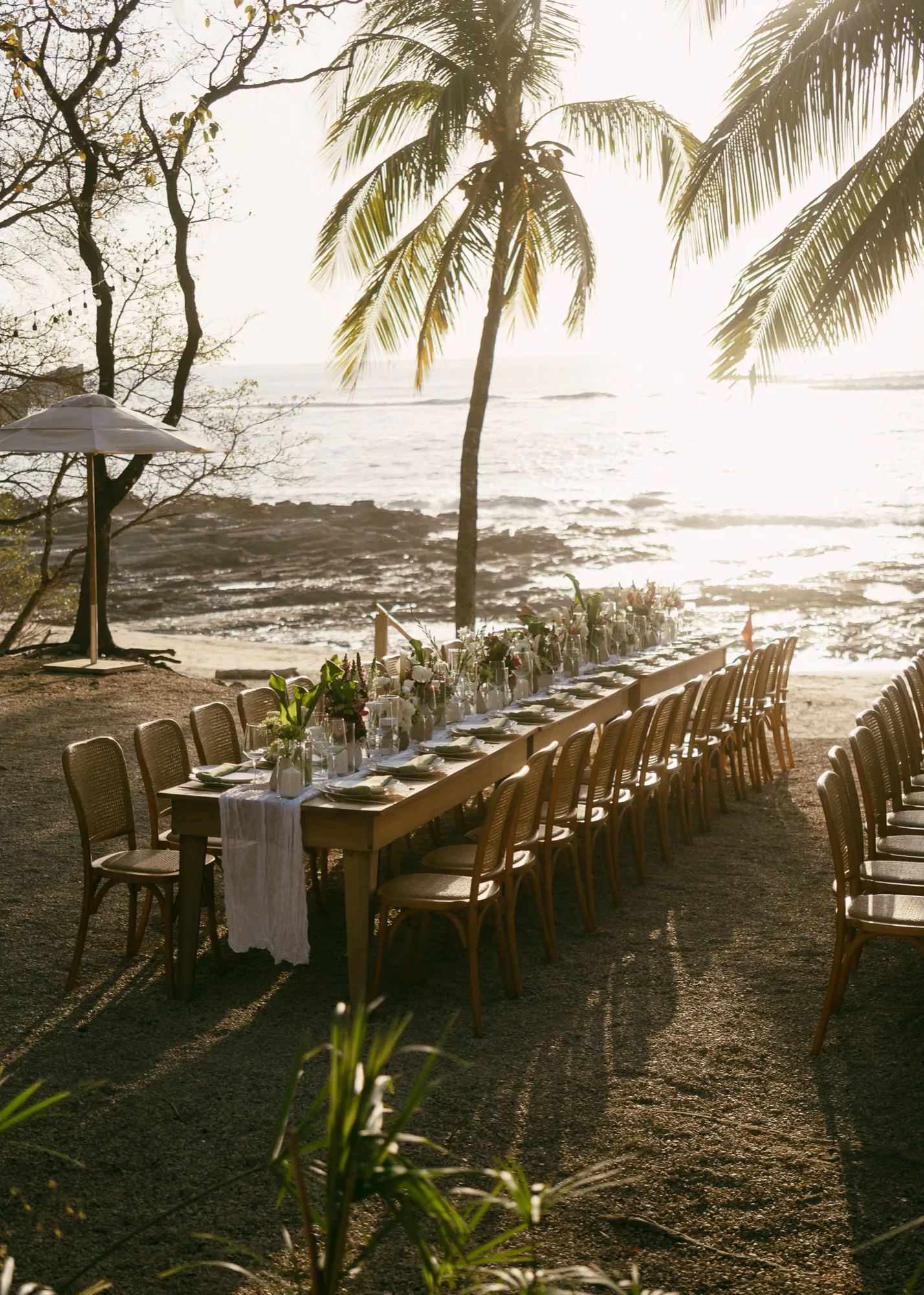 A long banquet table set for a beachfront dinner under the palms at sunset in Nosara