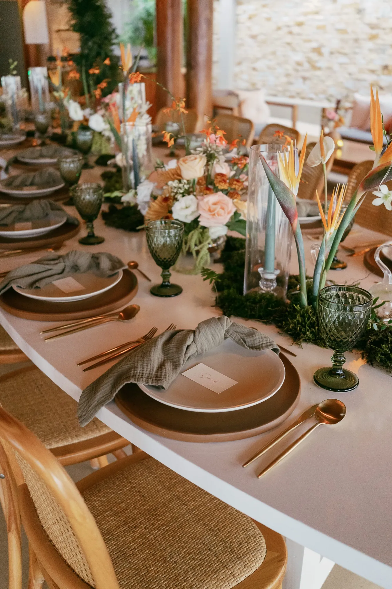 A styled reception table with matte ceramics, sage linens, copper flatware, and tropical florals