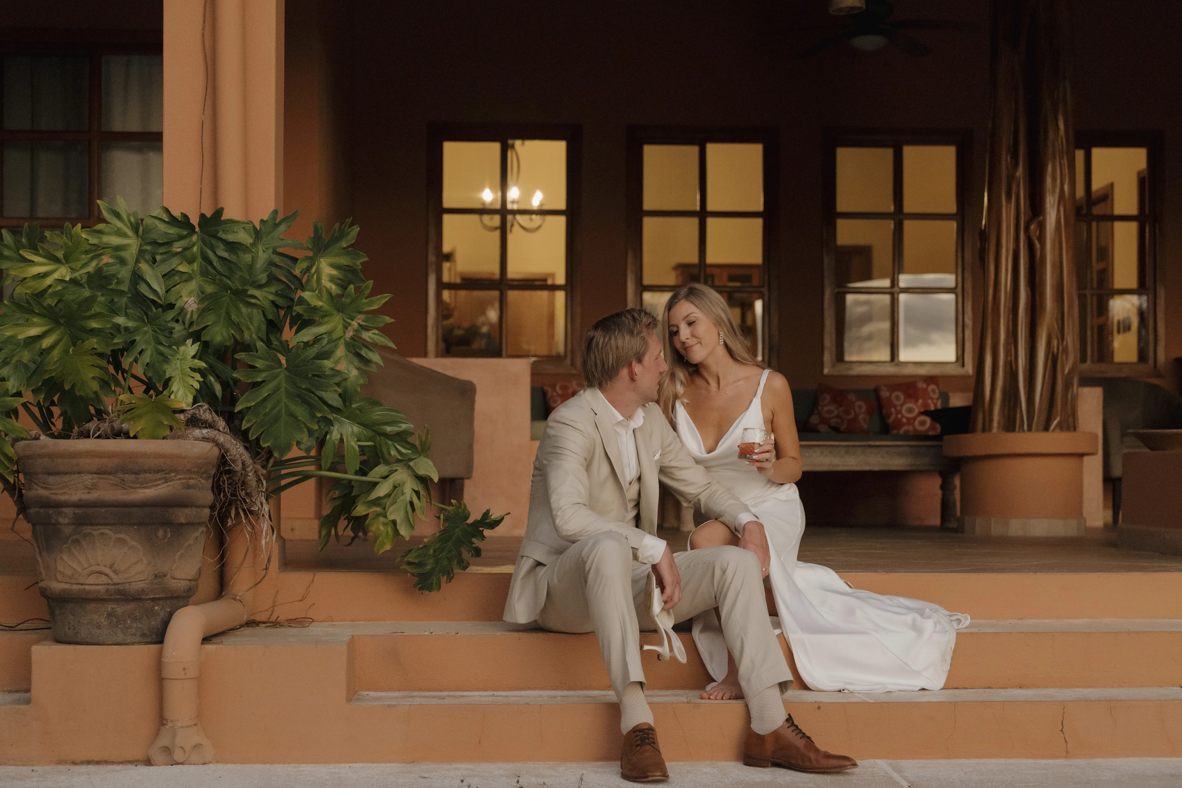 A couple sitting on the steps of a villa in Nosara at dusk, with the windows lit behind them