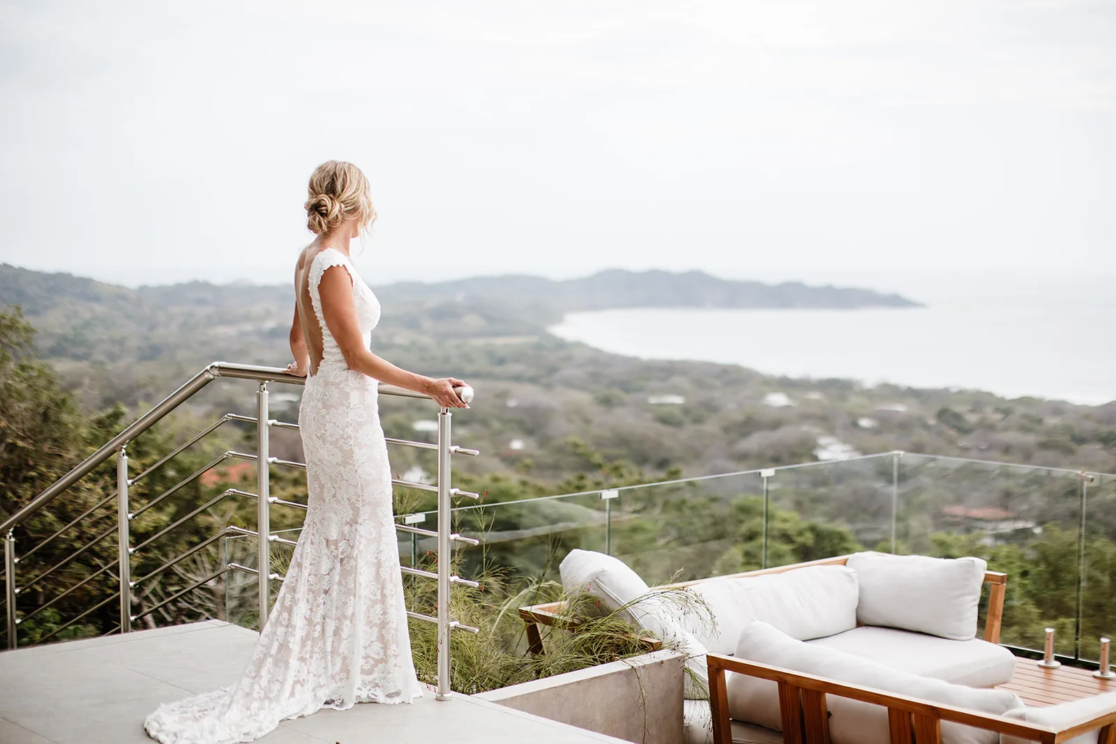 A bride standing on the terrace of a hilltop villa in Nosara, looking out over the jungle to the coastline