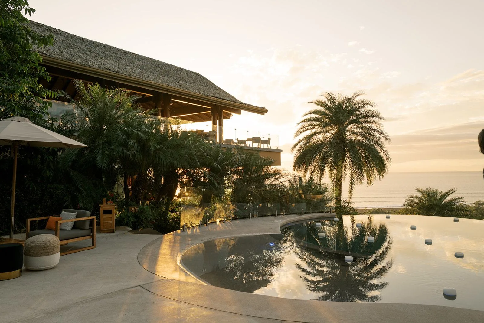 A poolside terrace at a Nosara villa at sunset, palms reflected in the water and lounge chairs set out for a welcome party