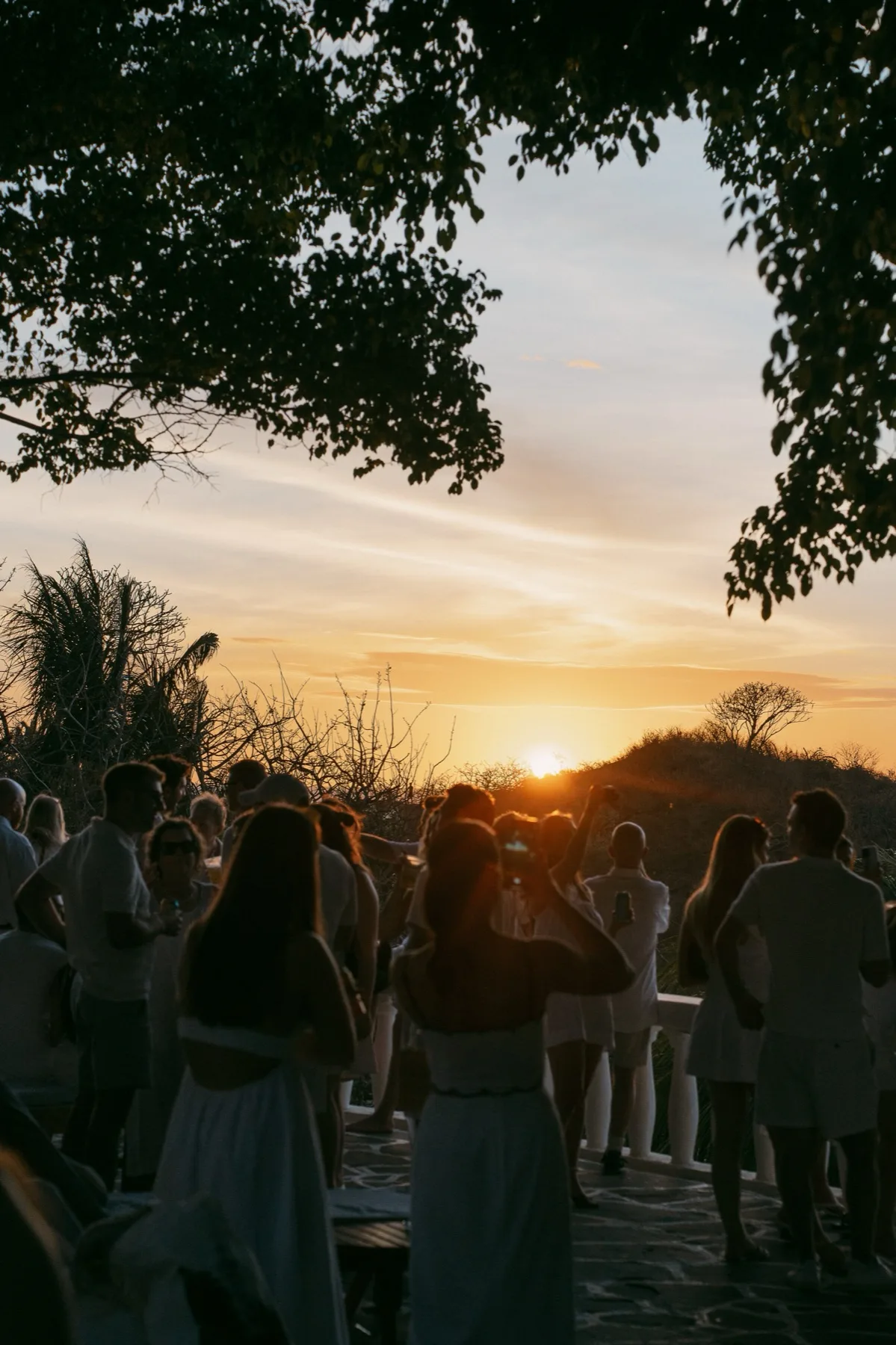 Wedding guests dressed in white watching the sun set over the hills at a Nosara welcome party